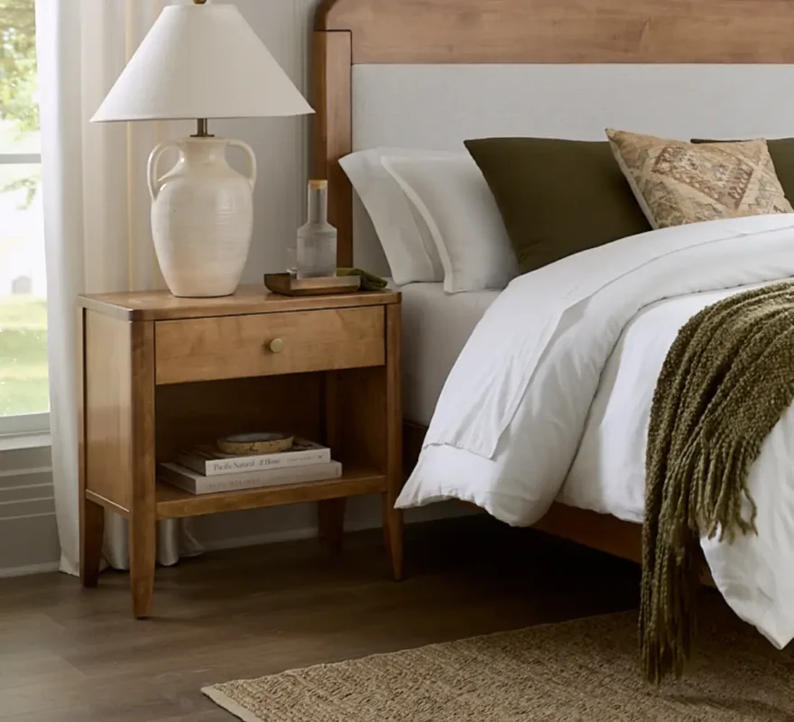 Mid-century modern wooden nightstand with a white ceramic lamp.