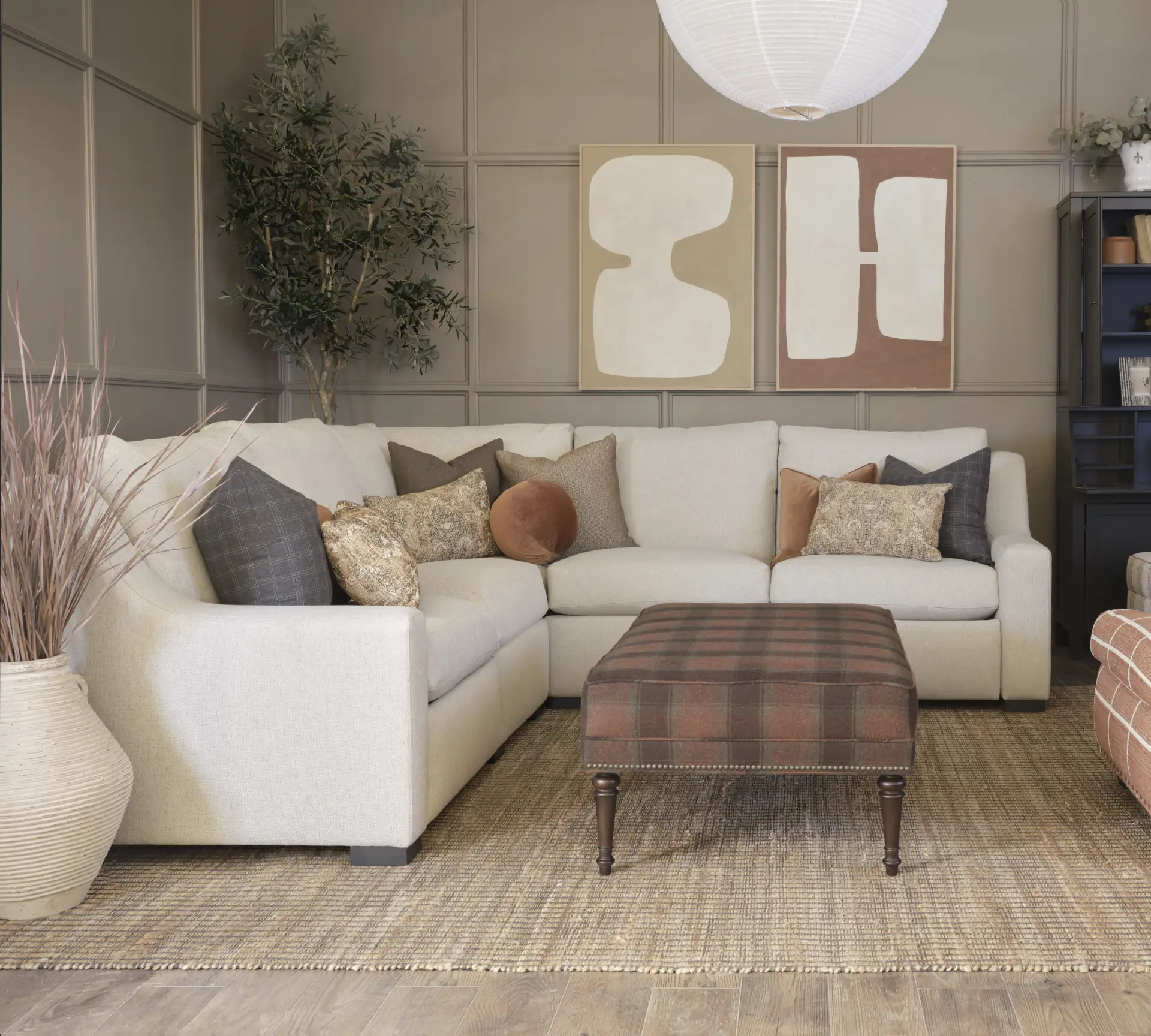 Cream sectional sofa with plaid ottoman in neutral living room.